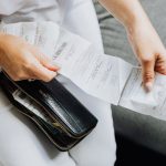 Mãos de uma mulher organizam vários recibos retirados de uma carteira preta.