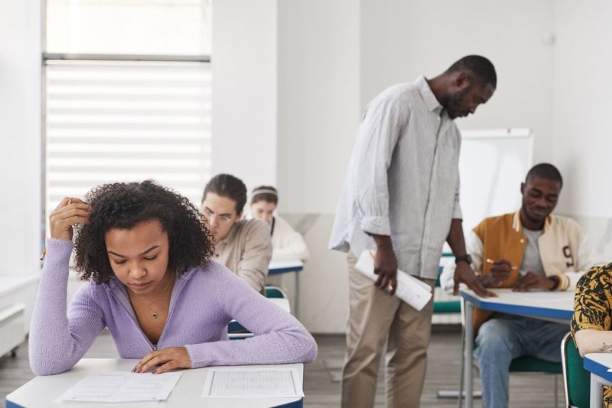 Estudantes fazem uma prova em sala de aula enquanto uma professora os supervisiona.