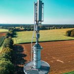 Vista aérea de uma torre de telefonia celular instalada entre áreas agrícolas e vegetação.