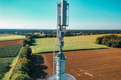 Vista aérea de uma torre de telefonia celular instalada entre áreas agrícolas e vegetação.