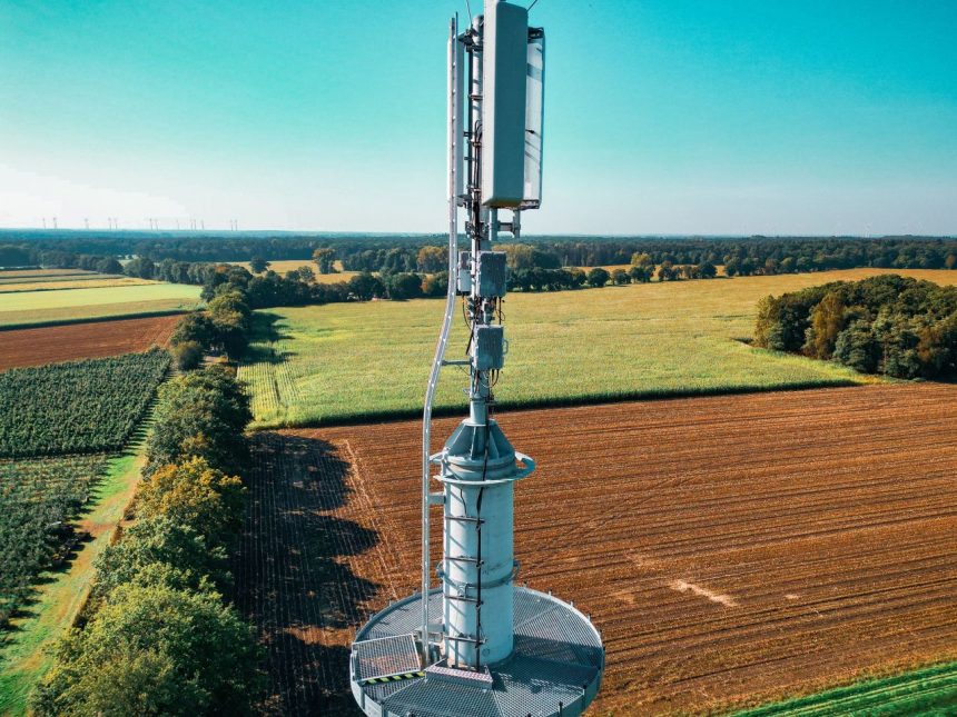 Vista aérea de uma torre de telefonia celular instalada entre áreas agrícolas e vegetação.