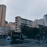 Pedestres e veículos atravessam uma rua movimentada de Belo Horizonte durante uma chuva intensa.