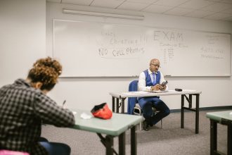 Fiscal acompanha estudantes durante a realização de uma prova em uma sala de aula.