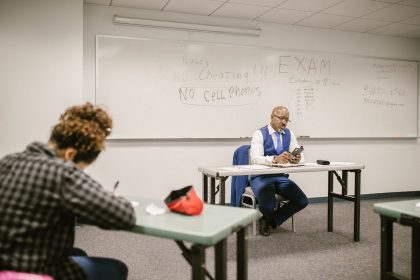 Fiscal acompanha estudantes durante a realização de uma prova em uma sala de aula.