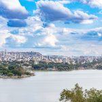 Vista panorâmica de Belo Horizonte com um lago cercado por vegetação sob um céu colorido