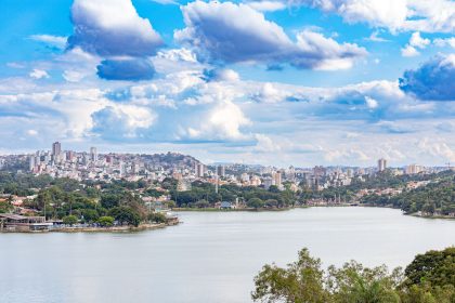 Vista panorâmica de Belo Horizonte com um lago cercado por vegetação sob um céu colorido