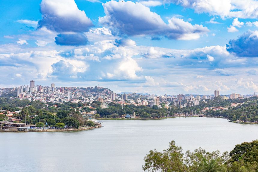 Vista panorâmica de Belo Horizonte com um lago cercado por vegetação sob um céu colorido