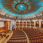 Plenário legislativo com assentos dispostos em semicírculo sob uma cúpula ornamentada.
