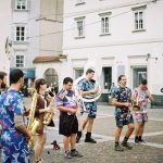Banda de rua se apresenta com instrumentos de sopro em uma praça urbana, diante do público.