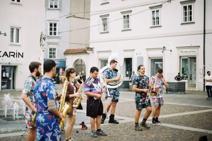 Banda de rua se apresenta com instrumentos de sopro em uma praça urbana, diante do público.