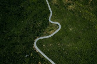 Vista aérea de uma rodovia sinuosa entre áreas verdes e montanhosas de Minas Gerais.