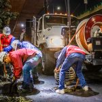 Trabalhadores fazem a limpeza de uma rede de drenagem urbana com máquinas, à noite, sob um viaduto.