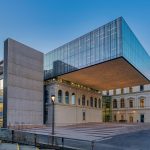 Fachada de um edifício universitário moderno, com amplas janelas e área arborizada à frente