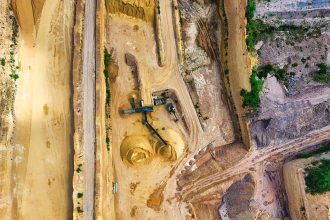 Vista aérea de uma mina a céu aberto, com máquinas e vias de circulação cercadas por áreas de vegetação.
