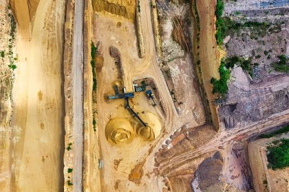 Vista aérea de uma mina a céu aberto, com máquinas e vias de circulação cercadas por áreas de vegetação.