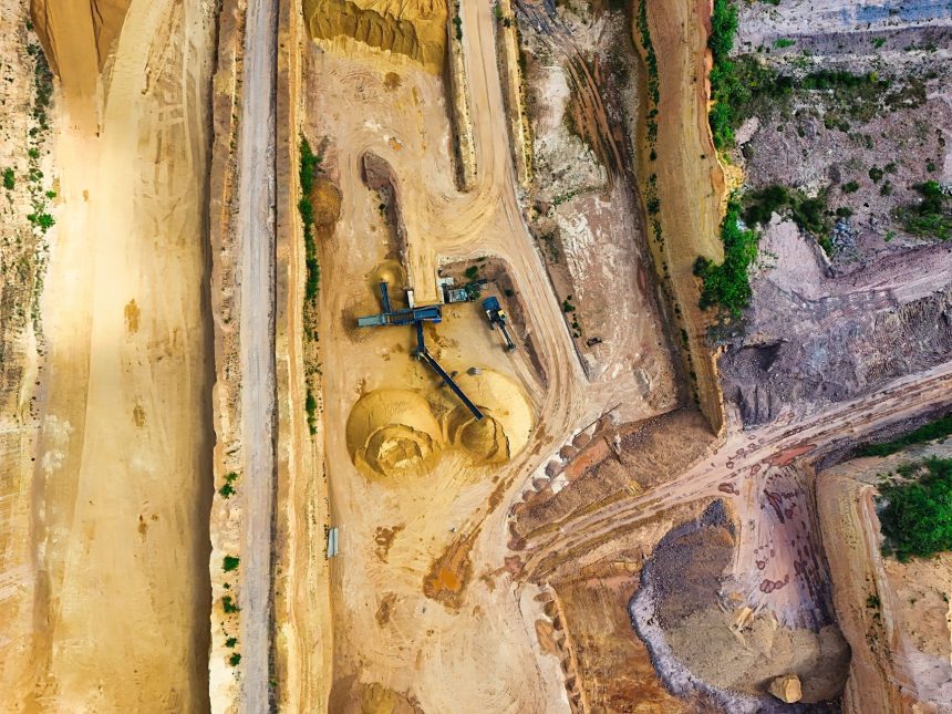 Vista aérea de uma mina a céu aberto, com máquinas e vias de circulação cercadas por áreas de vegetação.