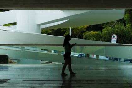 Silhueta de uma mulher caminhando em um espaço arquitetônico moderno enquanto consulta o celular.