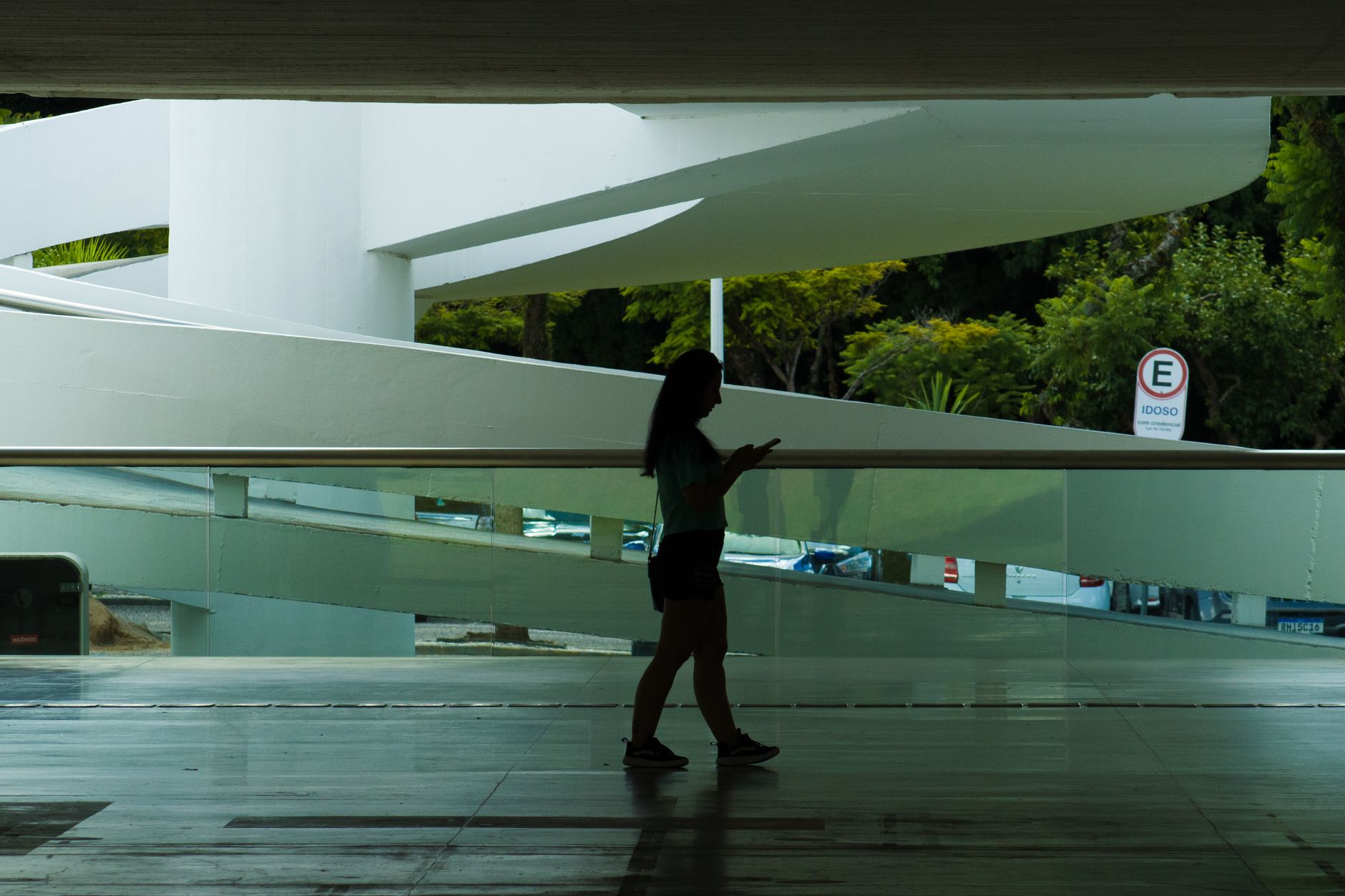 Silhueta de uma mulher caminhando em um espaço arquitetônico moderno enquanto consulta o celular.